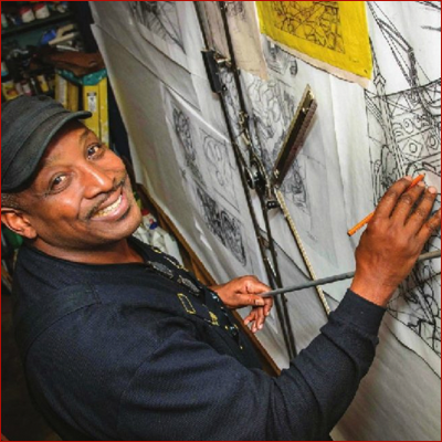 Man holding a pencil, appearing to work on a drafting table and smiling.