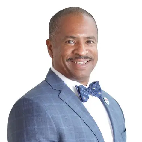 Man in a blue plaid suit and bowtie, smiling.