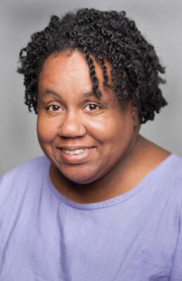 Woman with curly hair, wearing a purple top.
