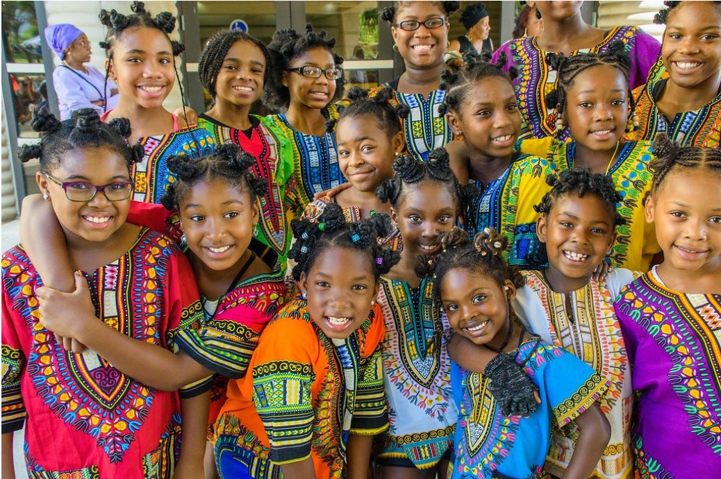 Group of colorfully dressed girls smiling with their arms over around each other.
