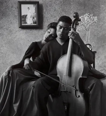 Black-and-white photograph of a man playing the cello while a woman leans on him