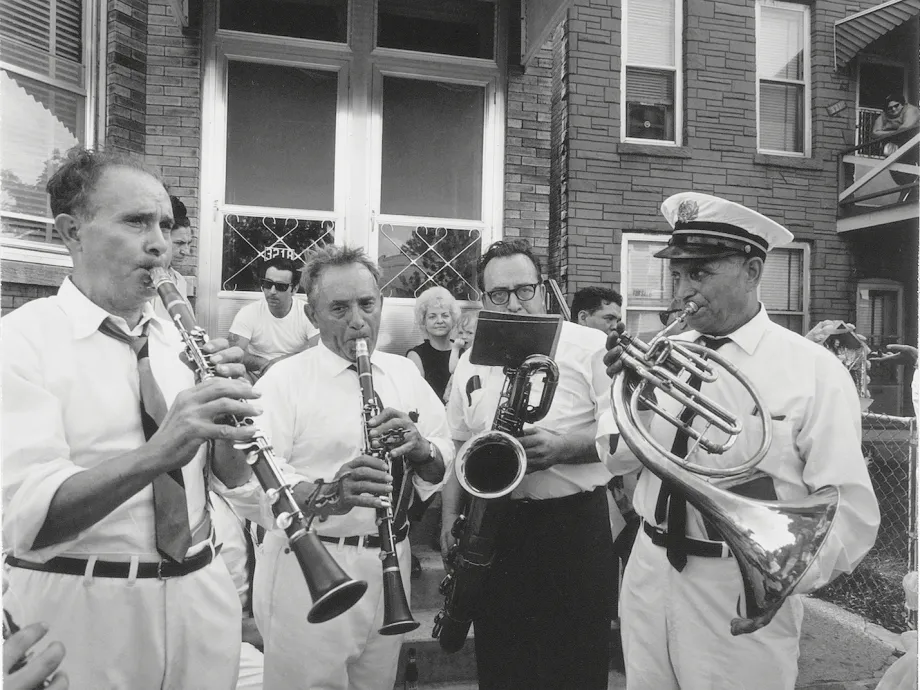 Black-and-white photograph of musicians playing for their neighbors on the sidewalk