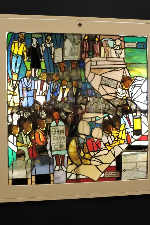 Stained glass piece depicting prominent black figures in history and signs meant to segregate.