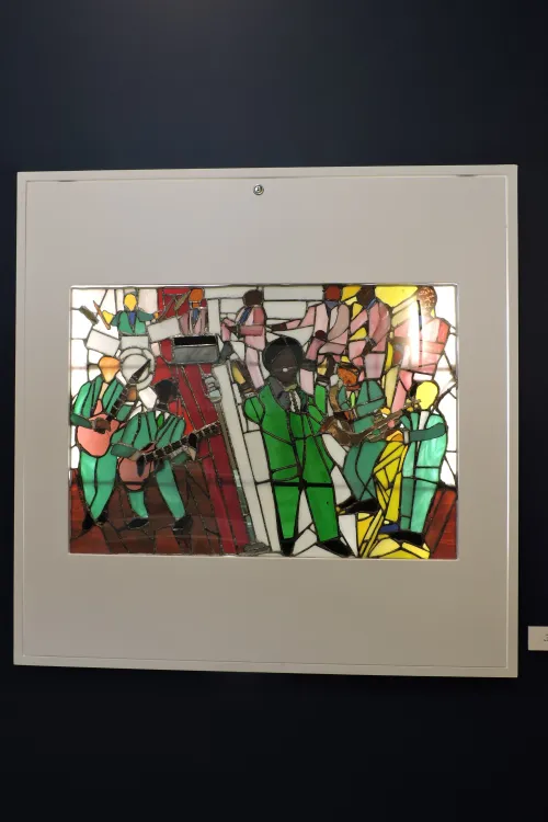 Stained glass piece depicting musicians in green suits performing on a red stage.